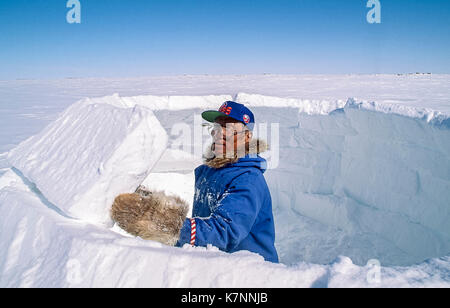 Aîné inuit homme, vêtu de vêtements modernes, s'appuie l'Arctique igloo en sculptant des blocs de neige et de les placer avec soin. c'est un abri traditionnel toujours utilisé par certains Inuits aujourd'hui Banque D'Images