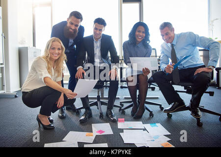 Portrait d'un groupe diversifié de dirigeants souriant avec brainstorming paperasse disposés sur le plancher d'un bureau moderne Banque D'Images