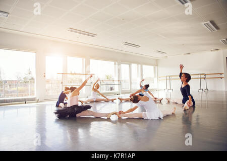 Ballerines peu assis et faire l'exercice de chaîne avec l'enseignant en classe de ballet. Banque D'Images