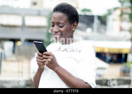 Jeune femme écrit des messages sur son téléphone portable et sourit. Banque D'Images