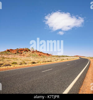 Longue route en courbe qui s'étend dans la distance dans la région de Pilbara en Australie-Occidentale, sous ciel bleu avec des nuages blancs. Banque D'Images