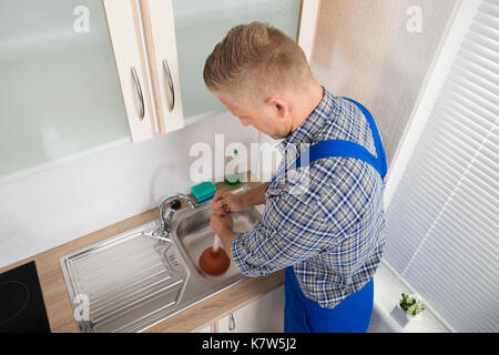 Plombier mâle en utilisant le poussoir dans évier en acier inoxydable dans la cuisine Banque D'Images