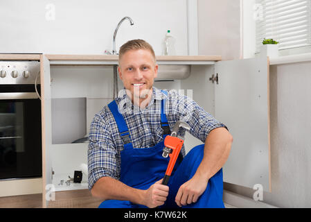 Happy plumber avec clé réglable assis dans la salle de cuisine Banque D'Images