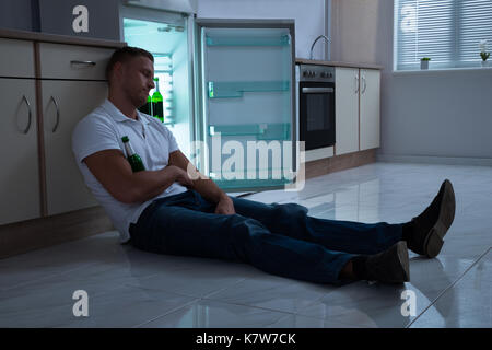 Jeune homme dormir avec une bouteille de bière dans la cuisine Banque D'Images