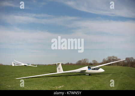 Deux planeurs au sol avec un troisième planeur remorqué dans l'air par un avion de remorquage. Storrington, West Sussex, Royaume-Uni Banque D'Images