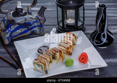 Théière et sushi set avec poisson anguille, source, le gingembre et le wasabi. Nigiri, maguro et rouleaux de sushi servi sur plaque blanche sur fond de bois sombre. Close up Banque D'Images