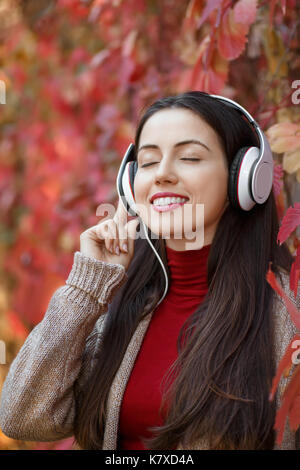 Young smiling woman in headphones aux yeux clos en plein air sur journée d'automne. girl listening music en parc. girl portrait automne apprécie la musique. Banque D'Images