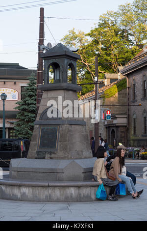 Deux japonaises assis sur le bord de la tour, place de la ville d'Otaru en pierre bleue avec les sacs, vestes et jeans. coucher de soleil sur les toits. Banque D'Images