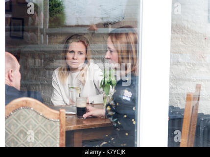 Vieux amis adultes ayant rencontre dans un pub. Tourné à travers la vitre en verre avec une réflexion sur l'orientation horizontale. Banque D'Images