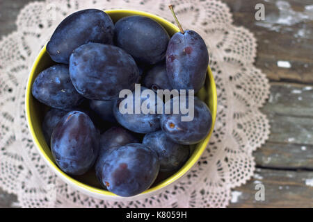 Vue de dessus les prunes en jaune bol, sur fond de bois Banque D'Images