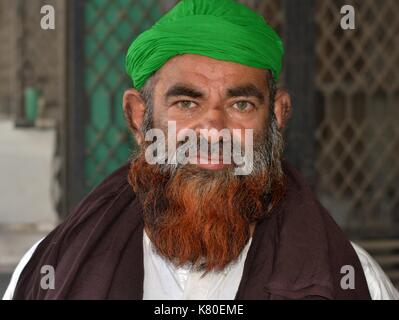 Un homme musulman indien âgé avec une barbe musulmane henné porte un turban vert et une prière brune et pose pour la caméra. Banque D'Images