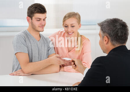 Mature Businessman Carte de visite donnant à Young Couple In Office Banque D'Images