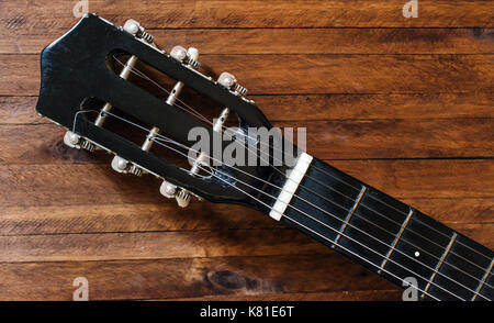 Guitare acoustique noire, tête de l'écrou, chevilles et cordes, sur une vieille table en bois brun, fond avec beaucoup de texture background et lignes Banque D'Images