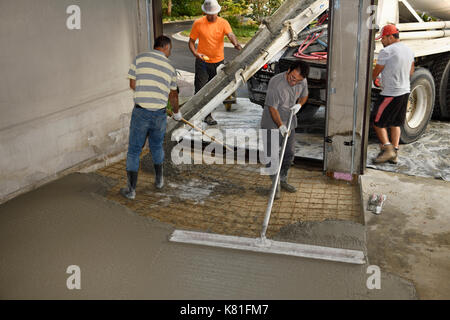 Verser de l'équipe de travail à partir d'un camion de ciment ciment chute sur un treillis métallique sur un plancher de garage résidentiel et la distribution avec grande truelle râteau et flotteur Banque D'Images