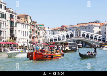 Occupé à la circulation des bateaux sur le Grand Canal au-dessous du pont du Rialto, Venise, Italie avec un gondolier touristes aviron en gondole, water taxi, travail barge tran Banque D'Images