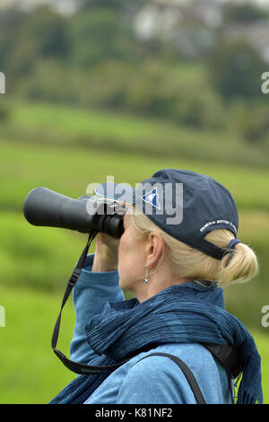 Une femme OU dame l'observation des oiseaux à la réserve naturelle rspb à brading marais sur l'île de Wight à l'aide de jumelles et guide de lecture.tics d'observation des oiseaux Banque D'Images