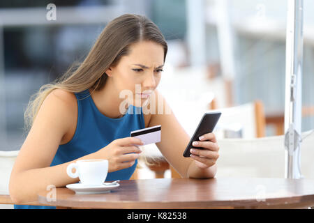 Seule fille inquiète des problèmes de payer en ligne avec une carte de crédit et d'un téléphone dans un café terrasse Banque D'Images