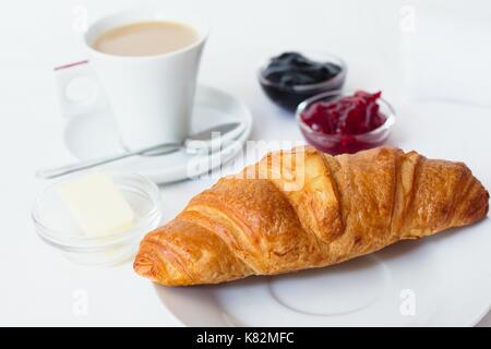 Croissant français frais servi avec des confitures, du beurre et une tasse de café avec du lait Banque D'Images