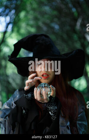 En sorcière avec chapeau noir magic ball en mains à la sombre forêt Banque D'Images