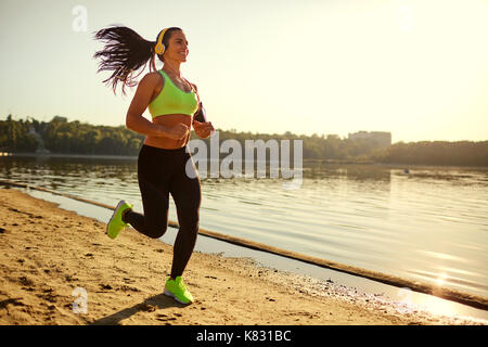 Une jeune femme runner s'exécute au coucher du soleil dans un parc dans le parc. Banque D'Images