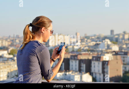 Femme à l'aide de son smartphone sur le toit avec vue panoramique de la ville en arrière-plan Banque D'Images