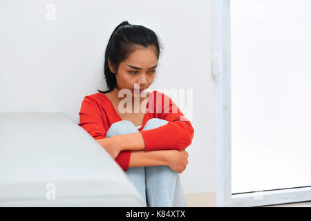 Portrait de femme assise asiatique triste et serrant genou s'appuya contre le mur Banque D'Images