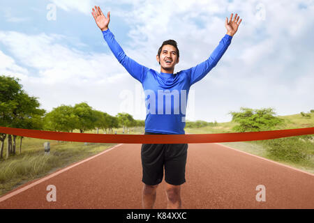 Portrait of asian man running de franchir la ligne d'arrivée sur la piste d'exécution Banque D'Images