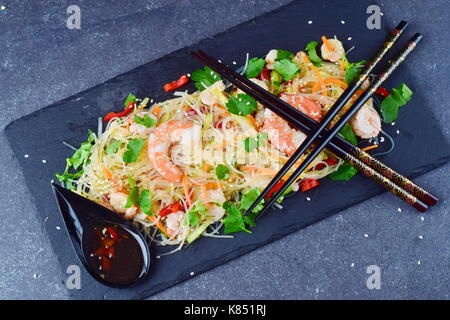 Nouilles aux crevettes et légumes sur une plaque en pierre noire avec la sauce orientale traditionnelle sur un fond abstrait gris. alimentation saine concept. Banque D'Images