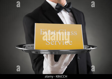 Close-up of waiter gant portant la plaque avec le texte de donner un service de première classe à bord Banque D'Images