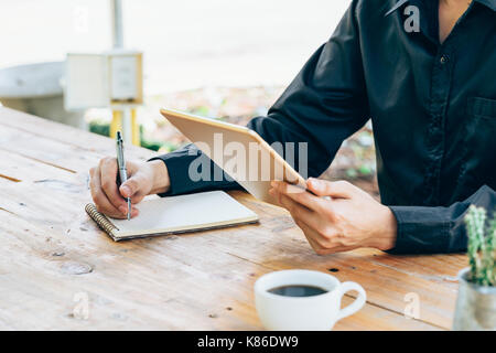 Business man hand holding tablet pc portable et de l'écriture dans un coffee shop. Banque D'Images