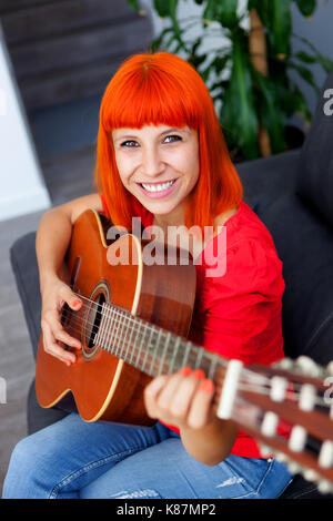 Femme redhaid détendue à jouer de la guitare dans sa maison. Banque D'Images