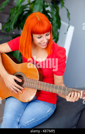 Femme redhaid détendue à jouer de la guitare dans sa maison. Banque D'Images