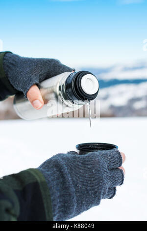 L'homme à l'aide de bouteille thermos sur la montagne enneigée Banque D'Images