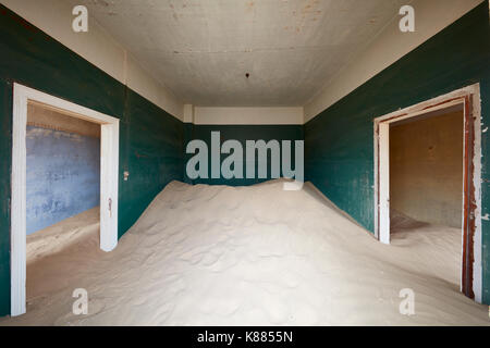 Un bâtiment abandonné, d'une chambre avec des murs peints et deux portes, et un tas de sable qui engloutit la moitié de la salle. Banque D'Images