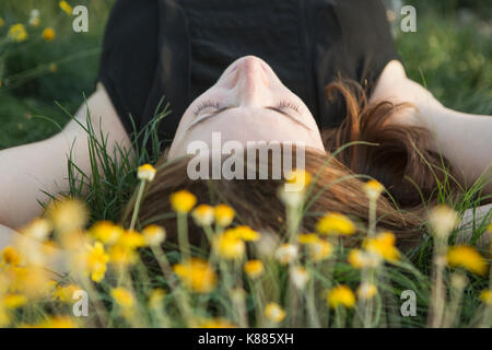 Une femme dans un débardeur noir et un jean couché dans l'herbe avec ses mains derrière sa tête. Banque D'Images