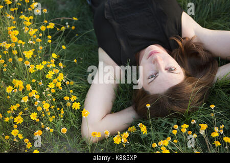 Une femme dans un débardeur noir et un jean couché dans l'herbe avec ses mains derrière sa tête. Banque D'Images