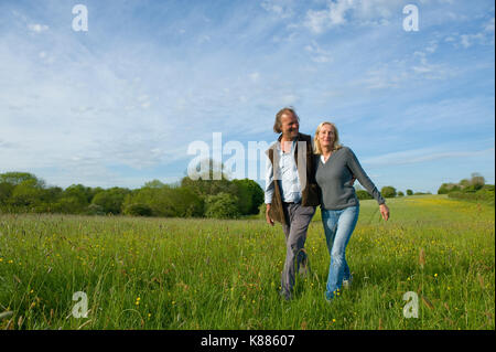 L'homme et de la femme marchant bras dessus bras dessous à travers une prairie. Banque D'Images