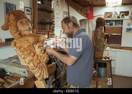 Un artisan sculpteur, travaillant sur une femme en bois de proue dans un atelier à l'aide d'un ciseau à bois. un travail en cours. Banque D'Images