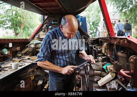 Blacksmith debout dans son atelier, une forge flottant sur une barge de travail 15-04, sur un objet métallique, à l'aide d'un fichier. Banque D'Images