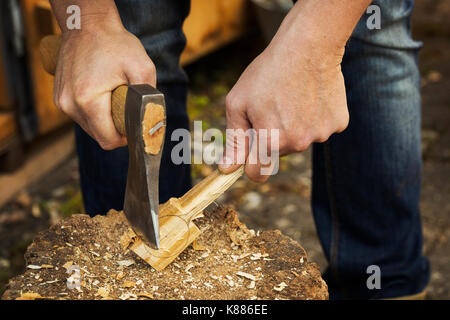 Close up de la main d'un homme tenant une hache, coupe et de façonnage d'un petit morceau de bois sur un bloc de séparation couvert de copeaux de bois. Banque D'Images