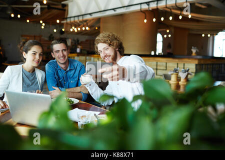 Cheerful young collaborateurs dans casualwear selfies prenant sur smartphone tout en ayant travailler réunion au café confortable petit Banque D'Images