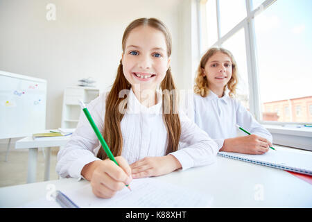 Smiling schoolgirl encombrement ou prendre des notes dans son cahier avec camarade près de par Banque D'Images