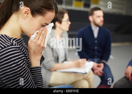 Crying woman wiping ses larmes avec un mouchoir avec groupmates communiquant sur arrière-plan Banque D'Images