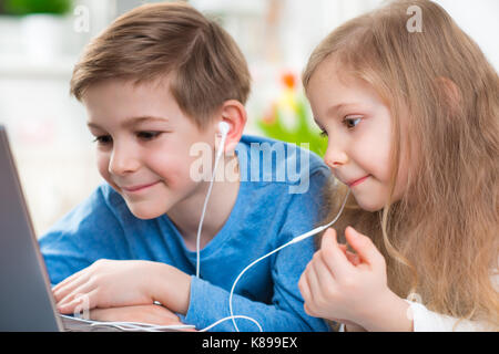 Deux heureux enfants jouant avec un ordinateur portable et d'écoute de la musique avec les écouteurs en double Banque D'Images