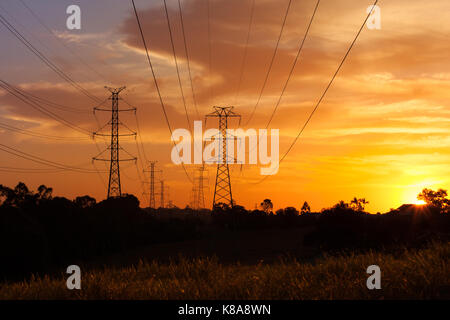 Une longue ligne de pylônes transportant l'électricité aux consommateurs sous un coucher de soleil spectaculaire. Banque D'Images