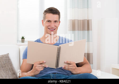 Portrait de jeune homme heureux avec album photo sitting on sofa Banque D'Images
