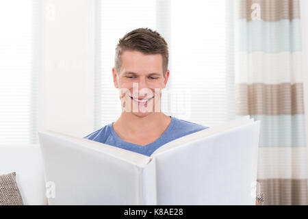 Portrait de jeune homme heureux avec album photo sitting on sofa Banque D'Images