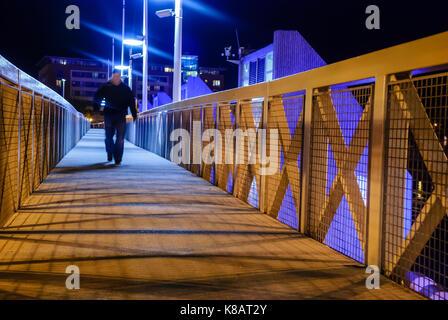 Un homme marche étendait sur toute une zone piétonne pont pied dans la nuit. Banque D'Images