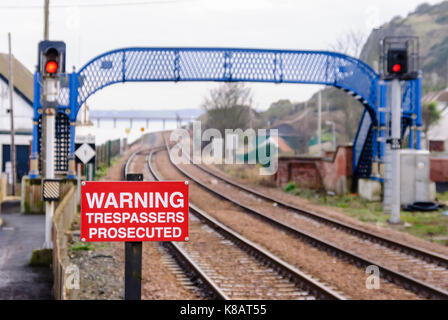 Panneau d'avertissement et d'une passerelle piétonne au-dessus des voies de chemin de fer. Banque D'Images