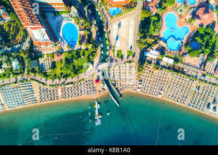 Vue aérienne de la mer turquoise transparente, belle plage de sable avec des chaises-longues, bateaux, arbres verts, piscine, hôtels, bâtiments au coucher du soleil en Banque D'Images